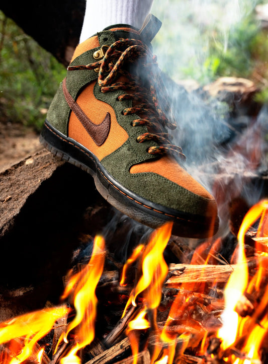 green and orange hiking boot inspired skate shoe behind campfire